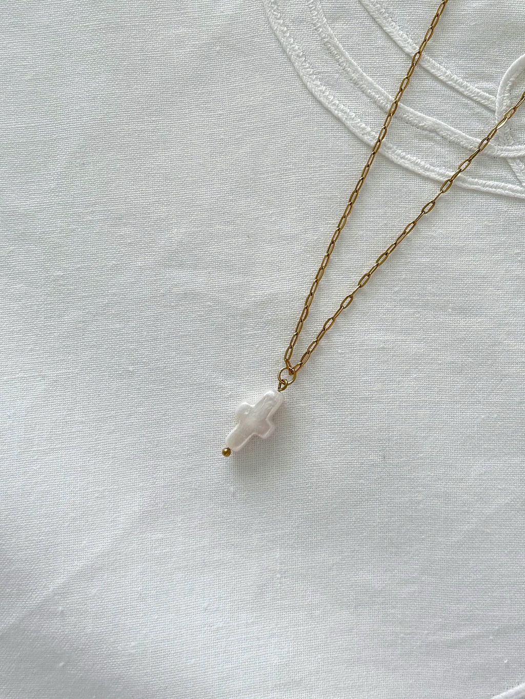 Freshwater pearl cross necklace displayed on soft neutral fabric