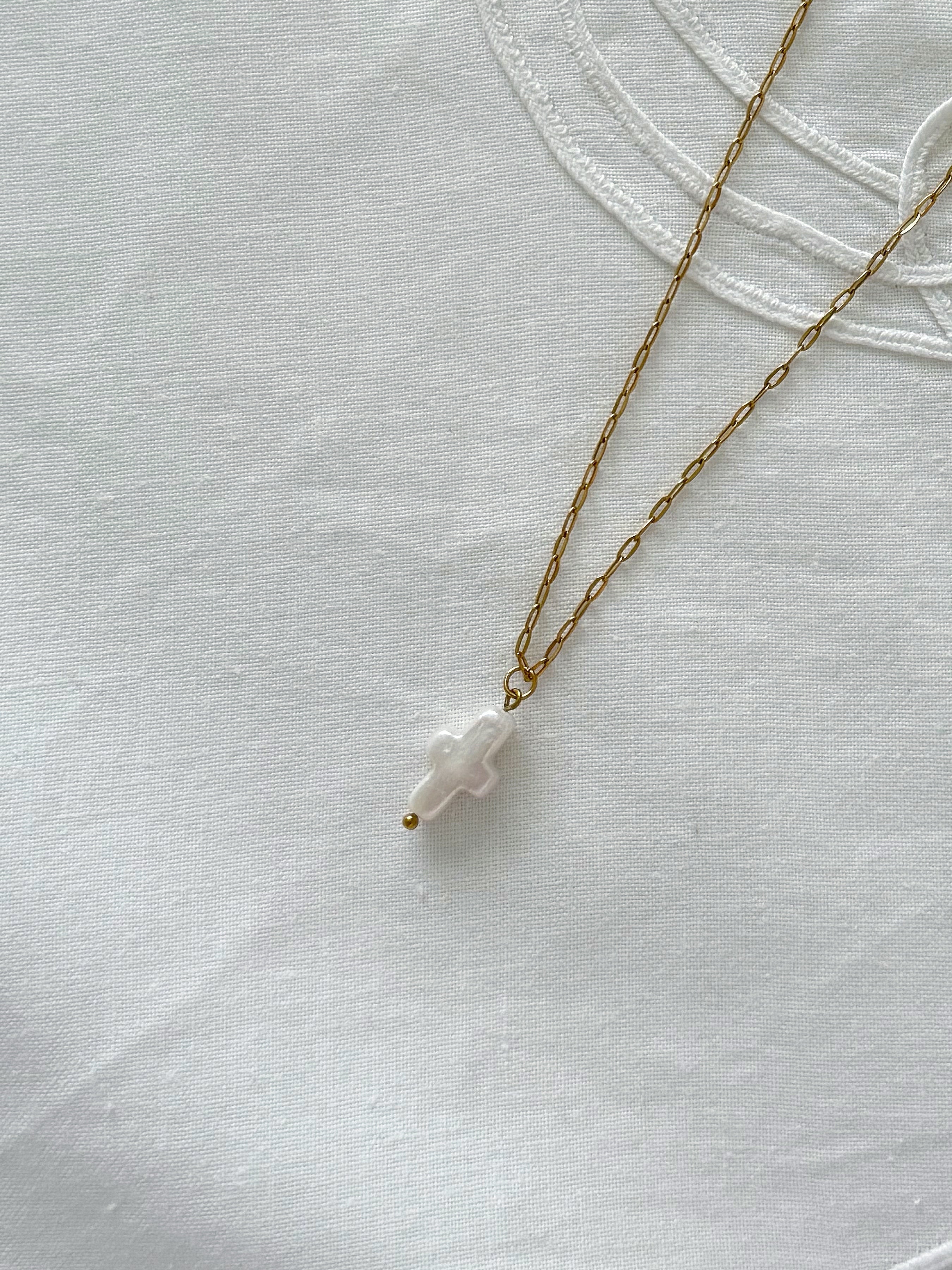 Freshwater pearl cross necklace displayed on soft neutral fabric