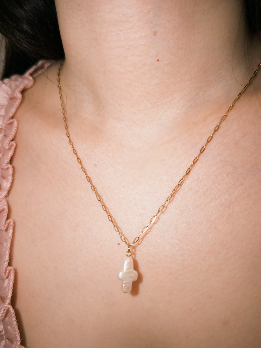 Minimal gold necklace with a freshwater pearl cross pendant in warm natural lighting
