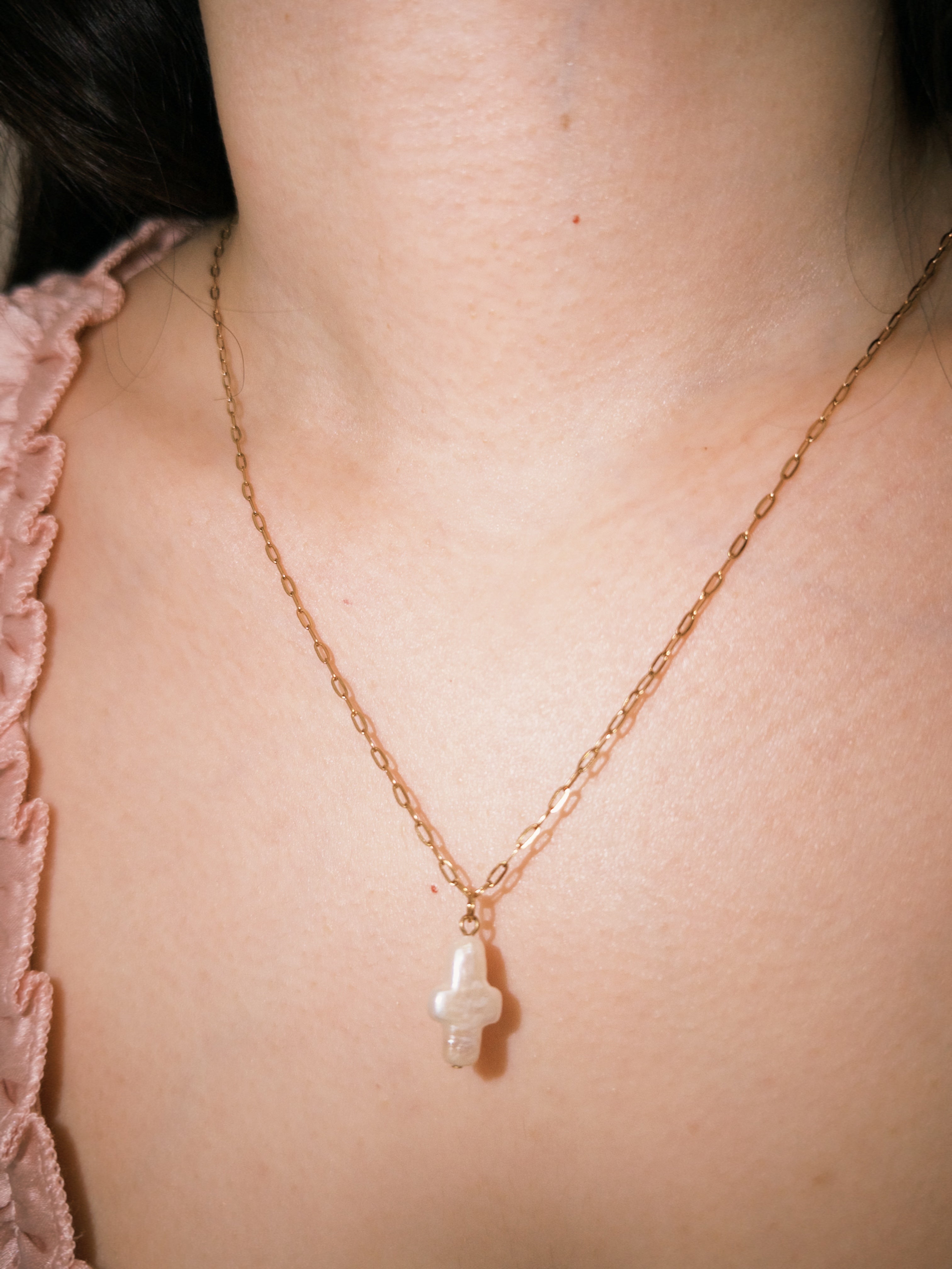 Minimal gold necklace with a freshwater pearl cross pendant in warm natural lighting