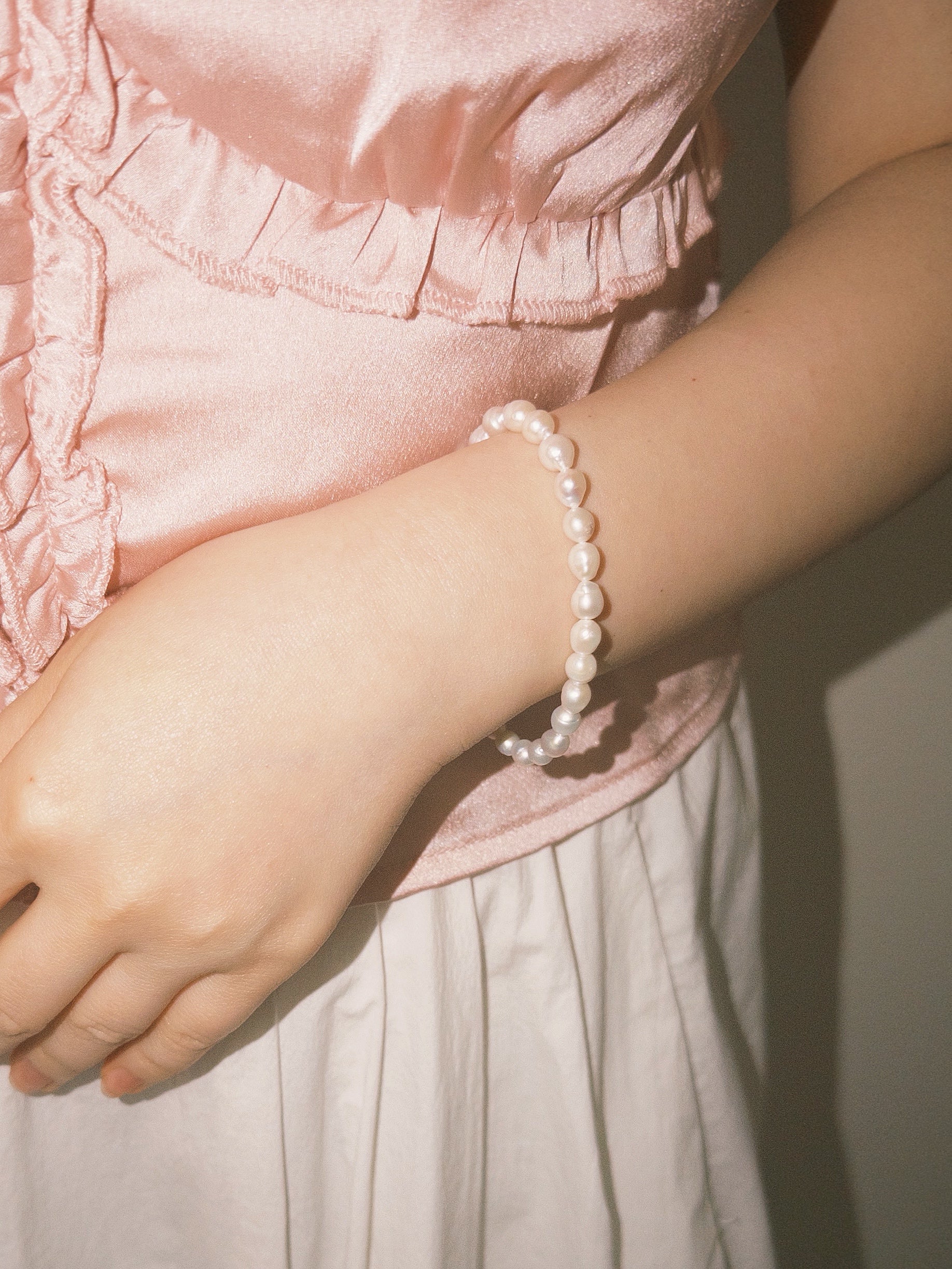 Minimal pearl bracelet paired with soft neutral textures in warm lighting