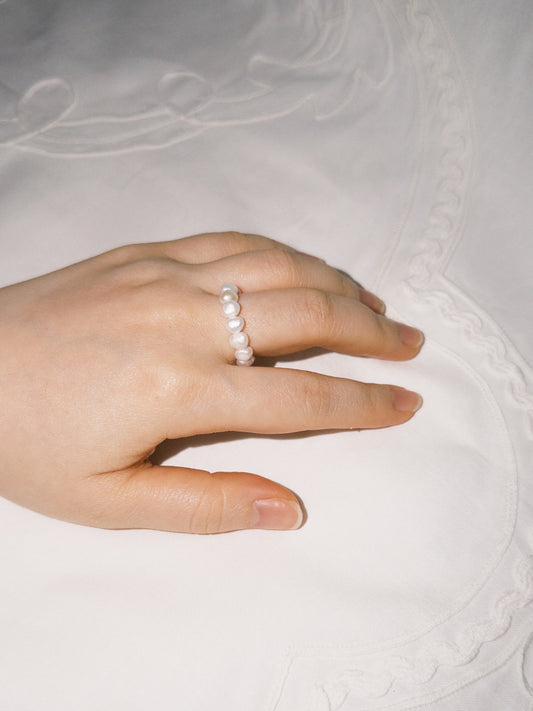 Minimal pearl ring styled softly in natural lighting