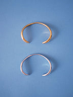 Minimal open cuff bracelets in gold and silver finishes on blue background